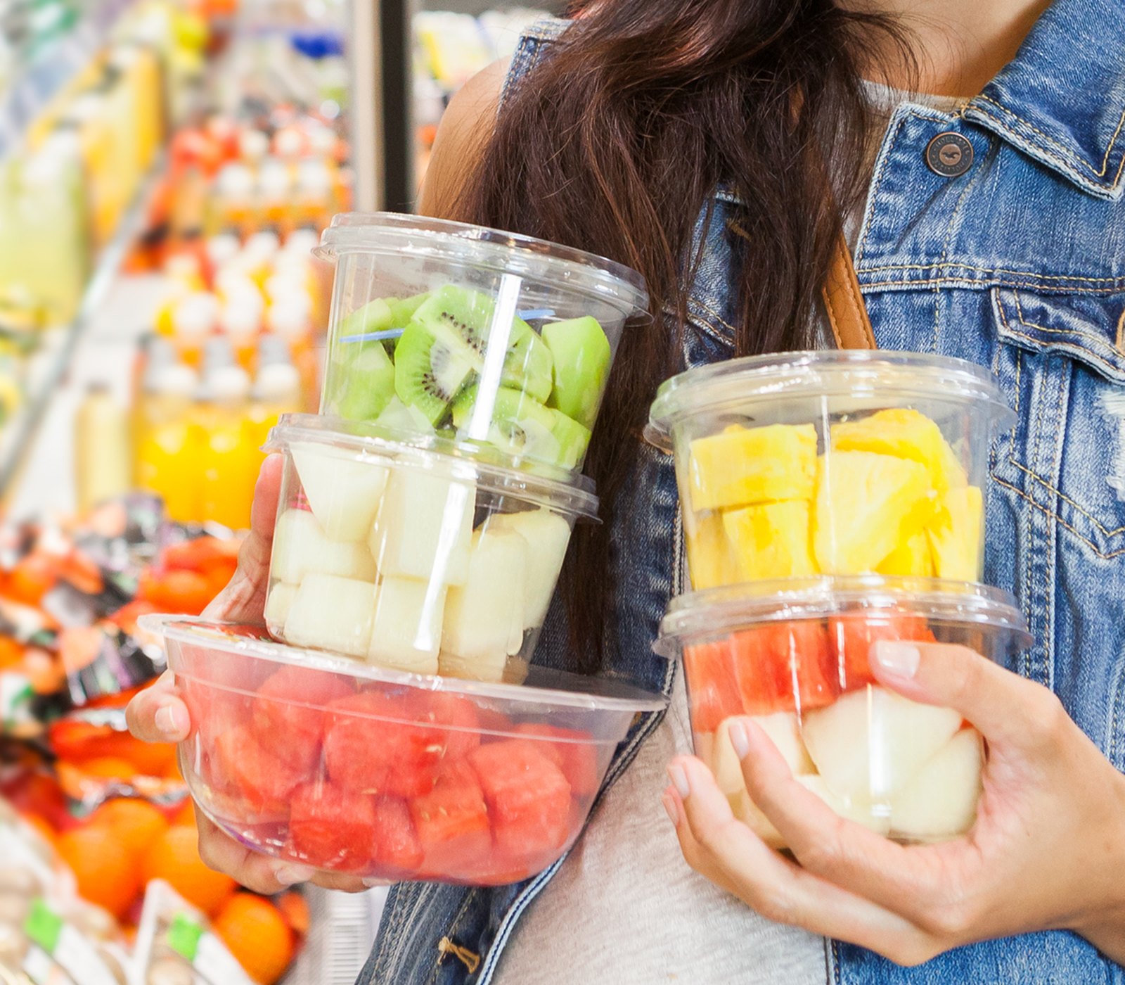 Clienta cogiendo dos tarrinas de fruta cortada en el lineal refrigerado del supermercado